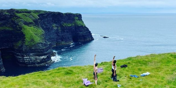 two people practicing yoga on the cliffs of moher, the sea can be seen in the background
