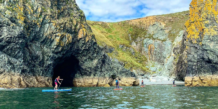 stand up paddle boarders out on the water by a cave and grassy coastline