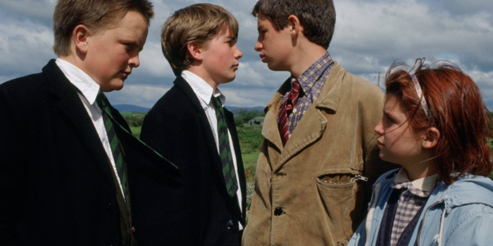 Still from War of the Buttons. Two boys in school uniforms face a taller boy in a brown jacket accompanied by a little girl with red hair.