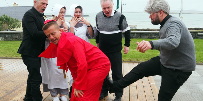 Man dressed as Bishop Brennan from Father Ted (red cloak and cap) being kicked up the arse by a man dressed as Father Ted (grey wig, grey jumper etc)