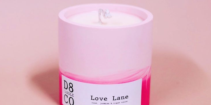 A candle inside a ceramic pot which is light pink on the top, darker pink on the bottom. Its white label reads "Love Lane"