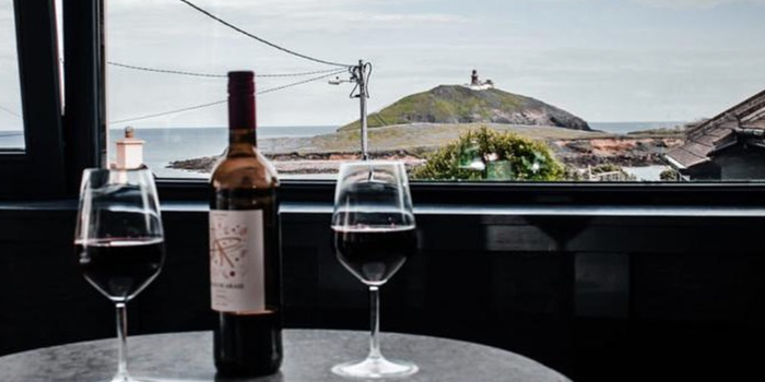 Red wine bottle with two glasses poured, a window in the background with sea view and an island with a lighthouse