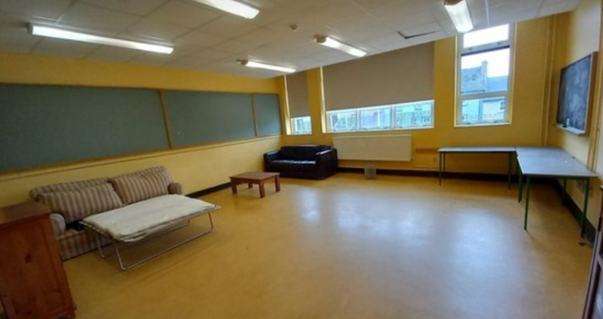 old classroom with yellow walls and chalkboards, empty apart from a sofa bed, small leather couch and fold out table in the corner