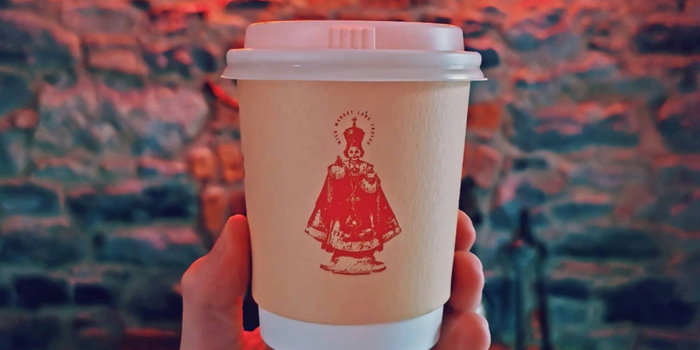 cream takeaway coffee cup with a red line illustration of the child of prague on the front