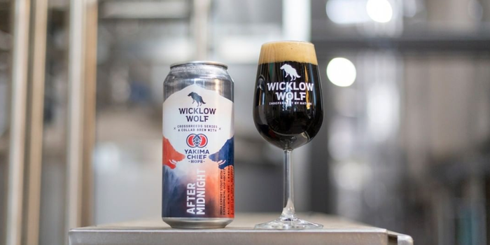 Can of Wicklow Wolf stout with small glass of the stout beside it. Out of focus, the brewery can be seen in the background
