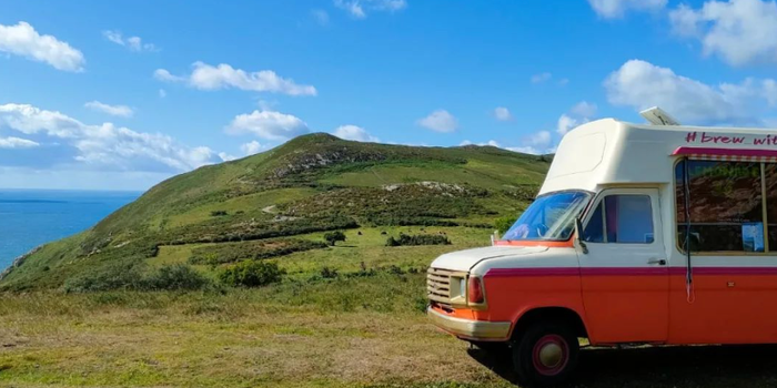 green field with a blue sky and orange and white coffee truck parked up