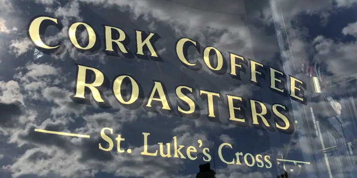 Window sign that reads Cork Coffee Roasters - St Luke's Cross, with the reflection of a cloudy sky in the window