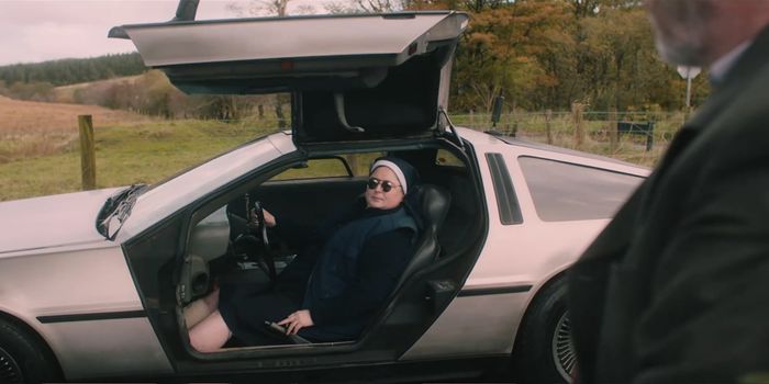 Sister Michael sitting in a delorean with the door open, wearing sunglasses