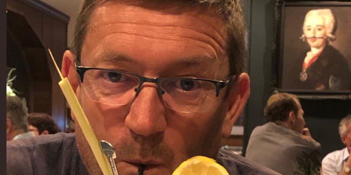 Man with glasses (paul heaton) drinking cocktail with straws and an orange slice decorating the glass