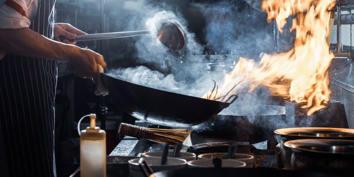 pan on a hob with flames coming from it on a hob in a restaurant kitchen, being tended to by a chef