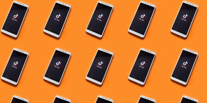 multiple phones on an orange background with the TikTok home screen showing on each phone