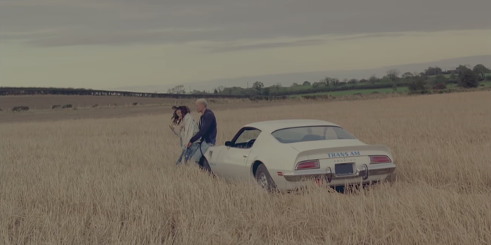 still from Rihanna's We Found Love Music video, Rihanna and her male co star in a barley field, leaning on a car