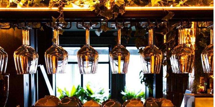 wine glasses hanging upside down on a rack in a restaurant, coffee machine underneath and window with sun shining through in the background
