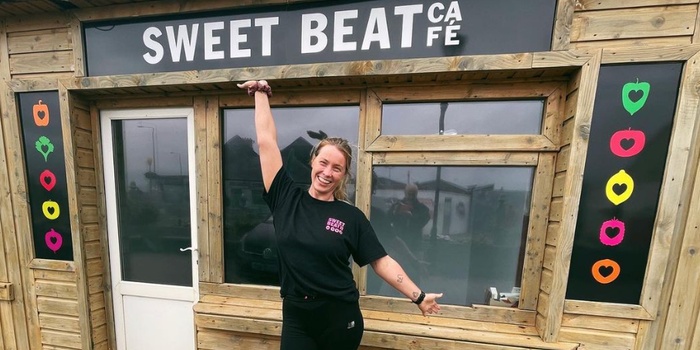 woman smiling outside a wooden panelled building with a sign reading "Sweet Beat Cafe"