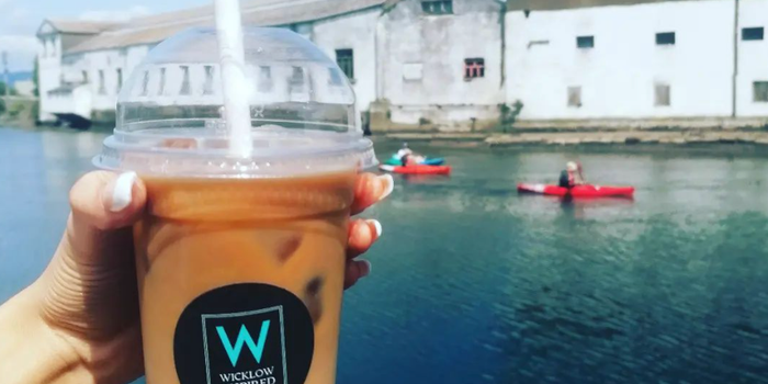 iced coffee cup being held out in front of a body of water with two people kayaking in the background