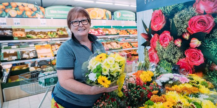 older woman with glasses smiling and arranging flowers at display in lidl