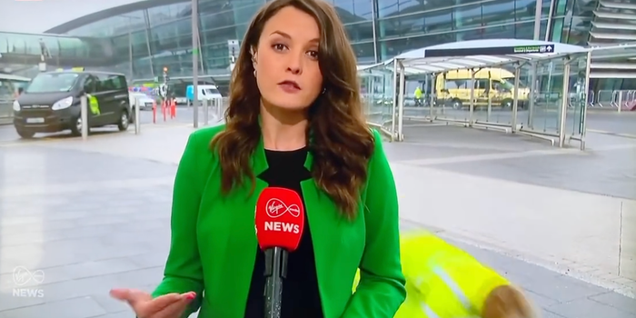 a newsreader speaking to camera at Dublin Airport with a man falling in the background