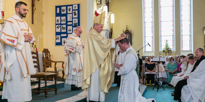 priest being ordained at a church, surrounded by other priests