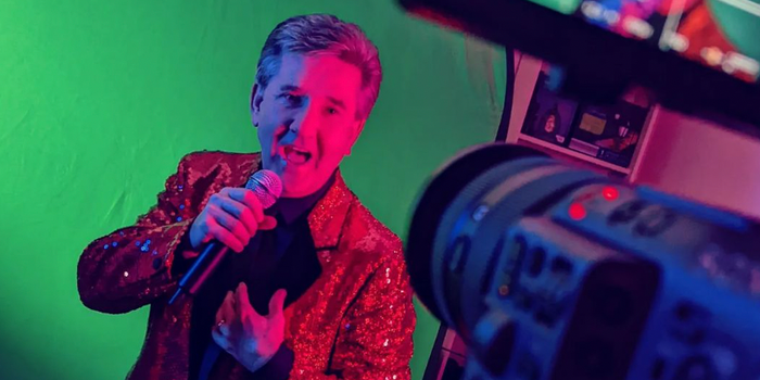 daniel o donnell singing into a microphone with a green screen behind him