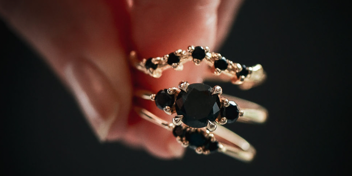 close up of a hand holding three gold rings with black diamonds
