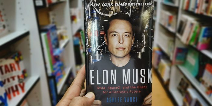 person in a bookshop holding up a book about elon musk