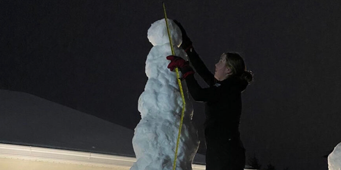 a woman standing beside a snowman with a tape measure to measure its height