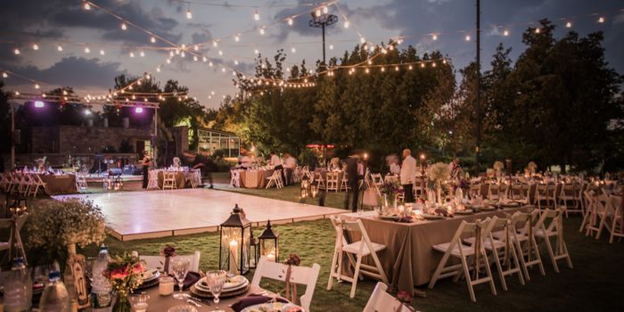 outdoor wedding scene in a field surrounded by trees, a dancefloor with tables and chairs and fairylights overhead