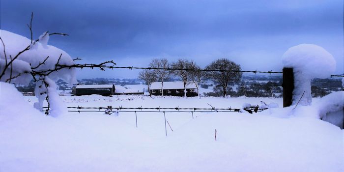 heavy snow on a wire fence surrounding a field